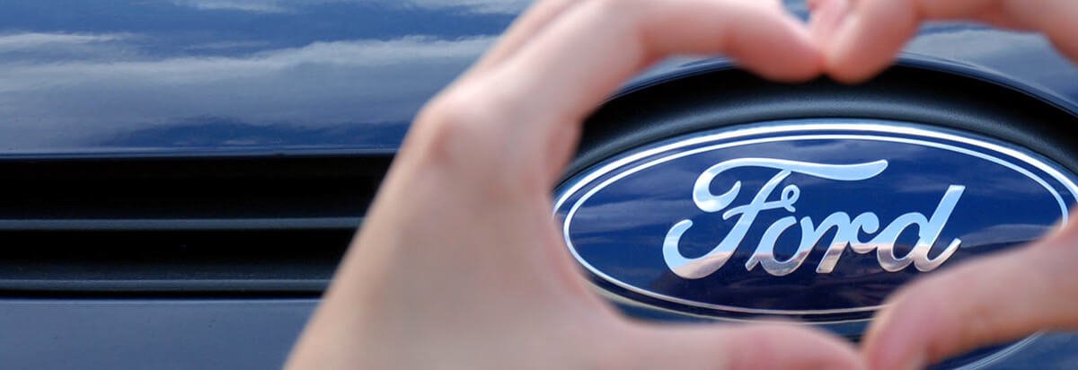 Die Hände formen ein Herz um das Ford-Logo auf einem blauen Hintergrund.