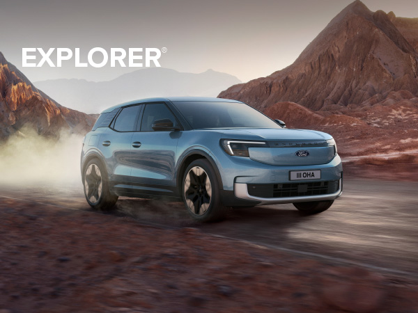 Ein blauer Ford Explorer fährt auf einer staubigen Straße in einer Berglandschaft.