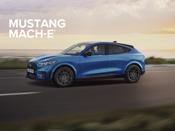 Ein blauer Ford Mustang Mach-E fährt auf einer Straße mit einem malerischen Hintergrund bei Sonnenuntergang.