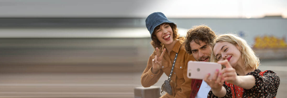 Drei junge Menschen machen ein Selfie im Freien, alle lächeln und posieren fröhlich.