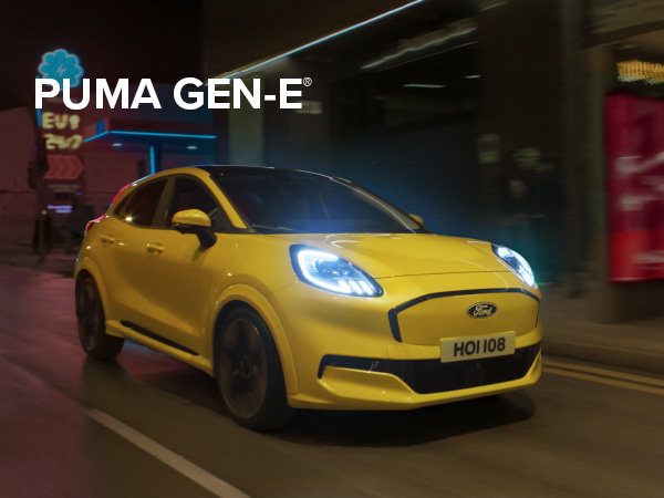 Ein gelber Ford Puma GEN-E fährt durch eine Stadtstraße bei Nacht, mit leuchtenden Scheinwerfern.