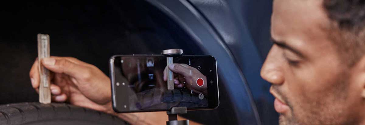 Ein Mann filmt mit seinem Smartphone das Messen der Profiltiefe eines Reifens mit einer Messlehre.